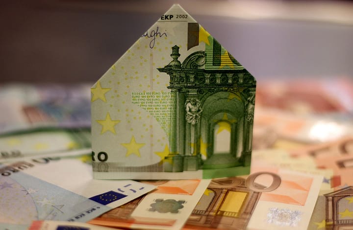 Ein gefalteter Geldschein in Form eines Hauses. Er soll die Kosten eines Strohballenhauses darstellen.